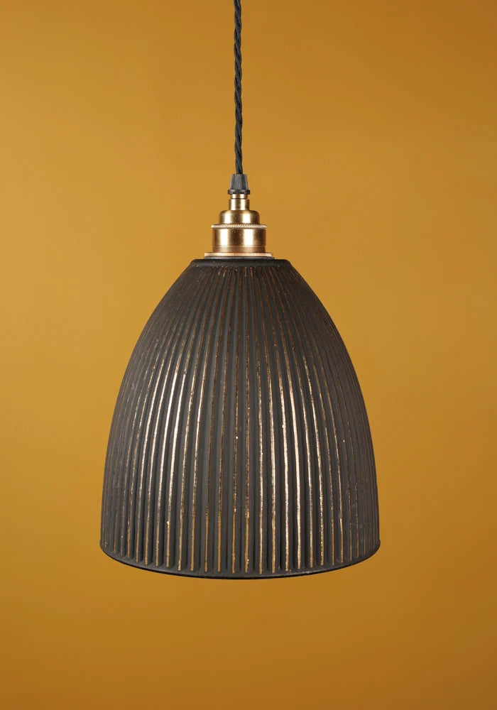 Black ribbed pendant light with brass lamp holder against a mustard yellow background