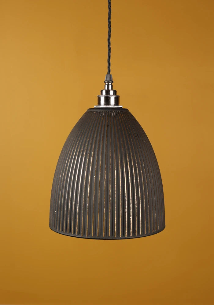 Black ribbed pendant light with nickel  lamp holder against a mustard yellow background