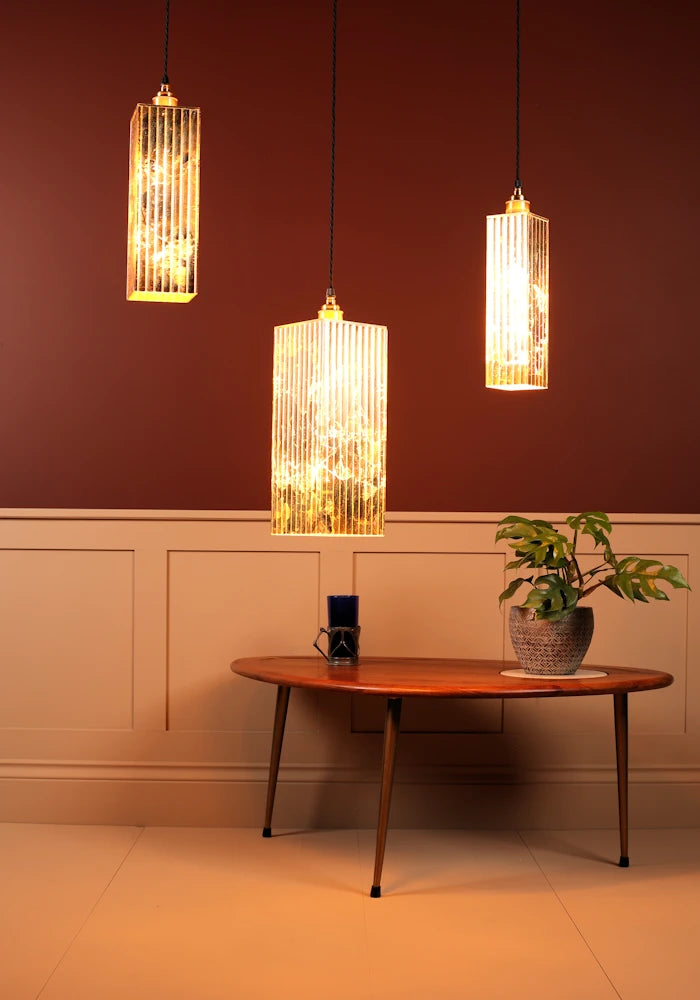 Three pendant lights hanging above a wooden table with a plant and small object in a room.
