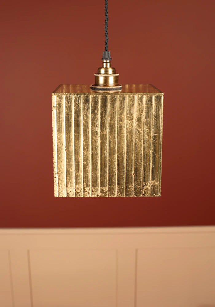 Close up of Gold leaf pendant cubed light with brass lamp holder, red and cream background