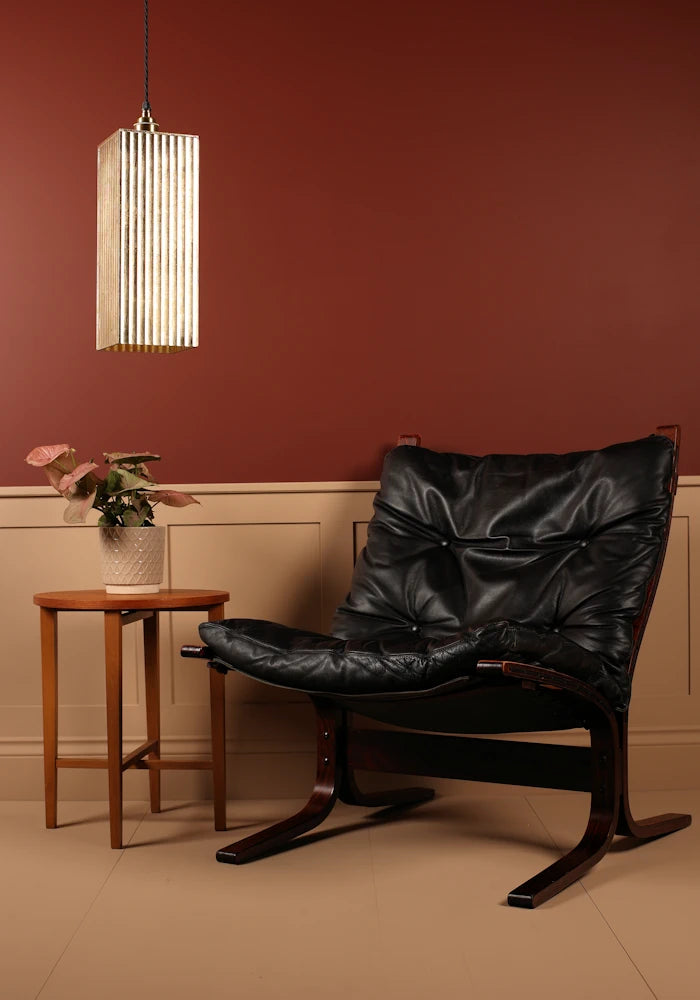 Large feature gold leaf pendant light, black leather chair in a room with a red wall and wooden side table.