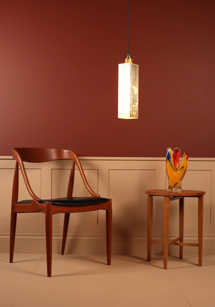 Wooden chair with black seat next to a small table with a colorful sculpture against a red wall.