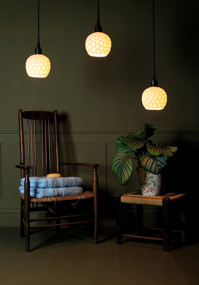 Triple cluster of beehive style porcelain bathroom pendant lights with wooden chair, bath towels and plant.