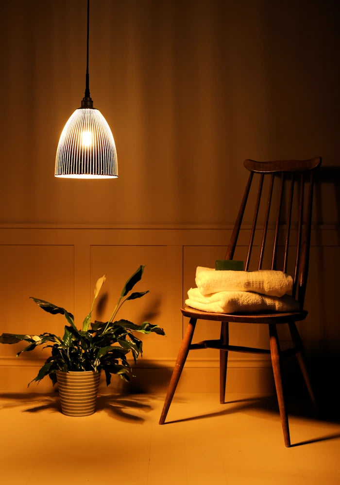 Black and gold bell shaped ribbed glass bathroom pendant light casting shadows onto plant and wooden chair 