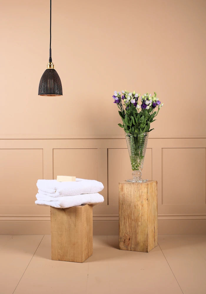 Small black and gold bell shaped ribbed glass bathroom pendant light switched off with towels and vase of flowers 