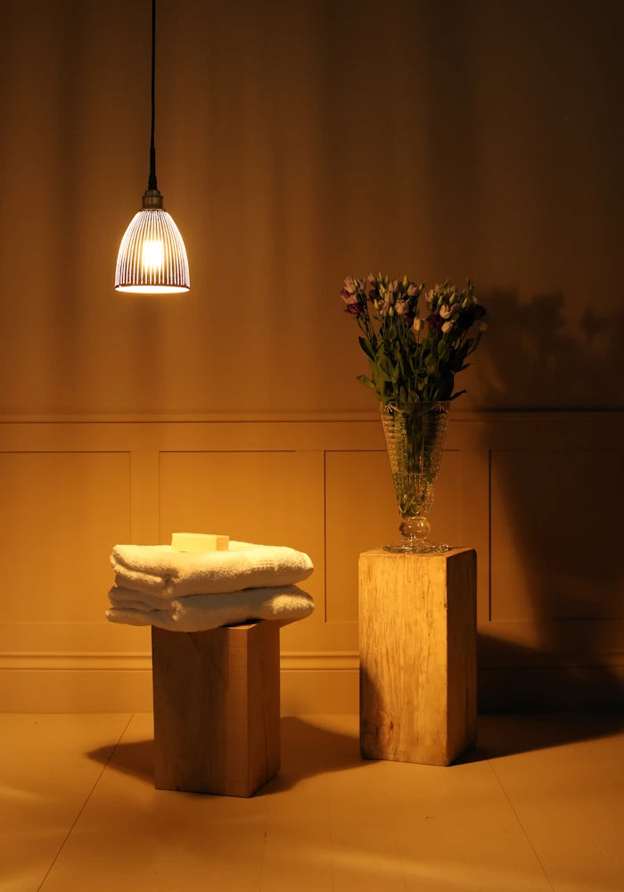 Small black and gold bell shaped ribbed glass bathroom pendant light casting shadows onto towels and vase of flowers 