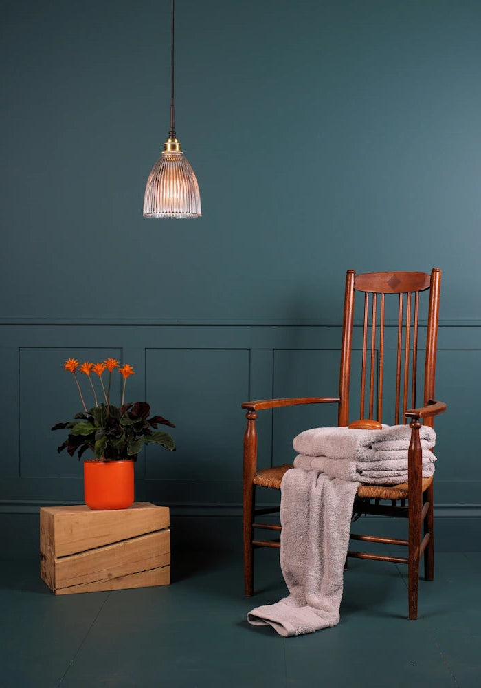 Small bell shaped glass bathroom pendant light switched off with wooden chair and orange flowers