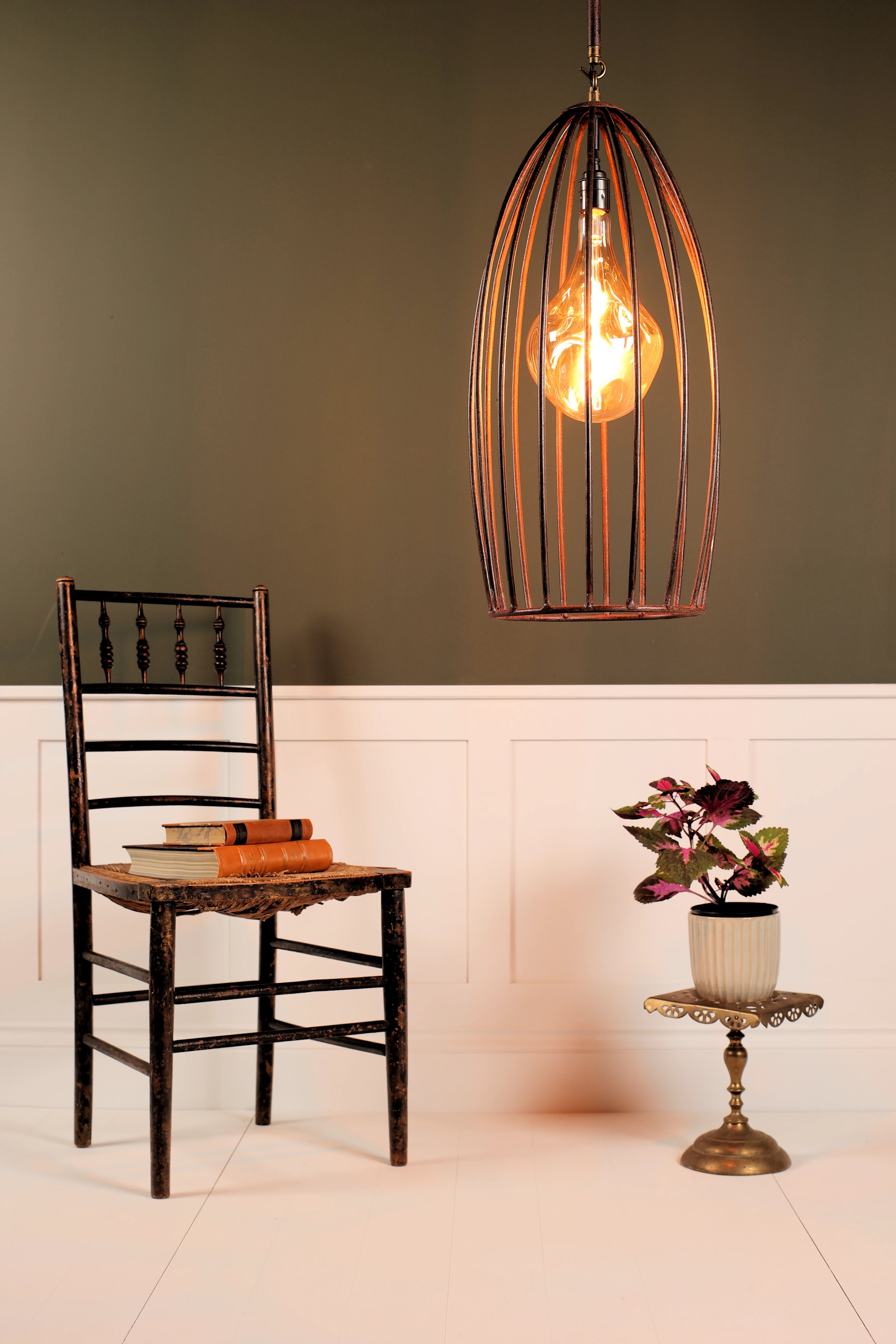 Vintage-style pendant light hanging above a wooden chair with books and a plant in a room with a green wall.