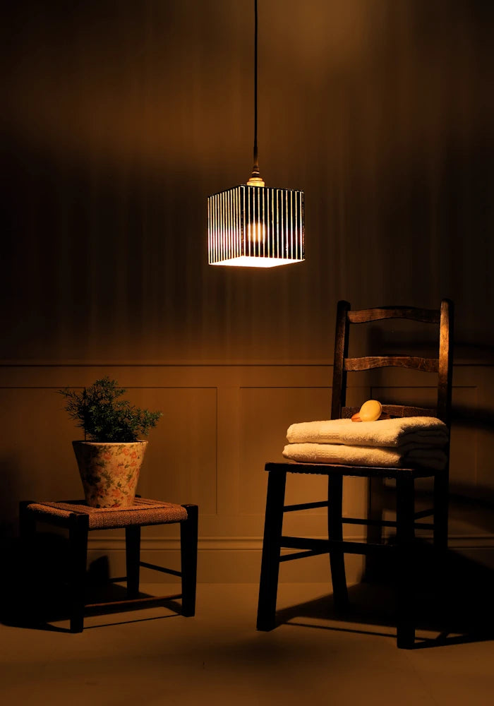 Ribbed glass black and gold leaf bathroom pendant light casting shadows onto plant, wooden chair and bath towels.