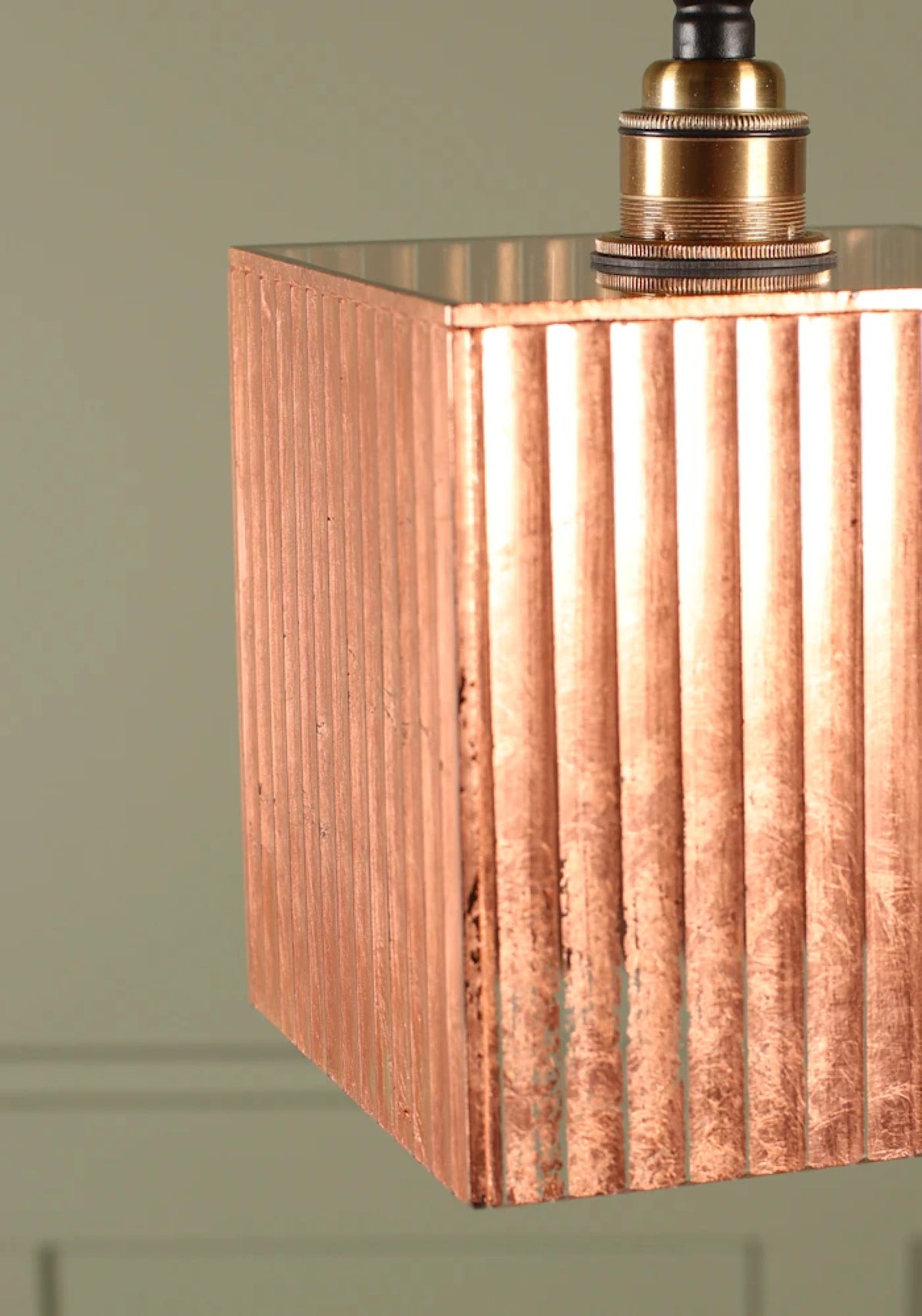 Close-up of a hanging pendant light with a square copper-toned shade featuring vertical fluted ridges and a brass-colored metal top fitting.