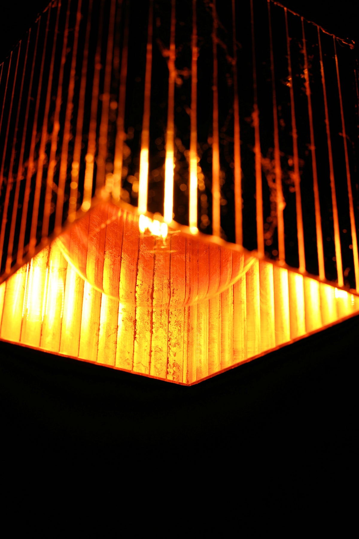 A close-up of a hanging pendant light fixture with a ribbed glass shade glowing warm orange and yellow against a dark background.
