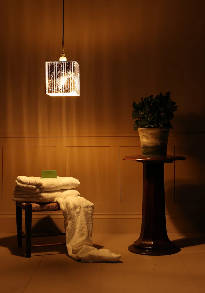 Large cube gold leaf bathroom pendant light with bath towels and plant on a stand.