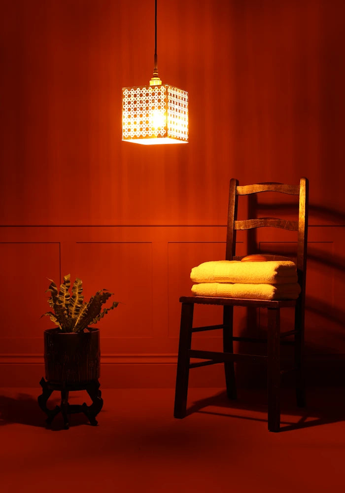 Large square Moroccan patterned gold bathroom pendant light, plant and wooden chair with towels.