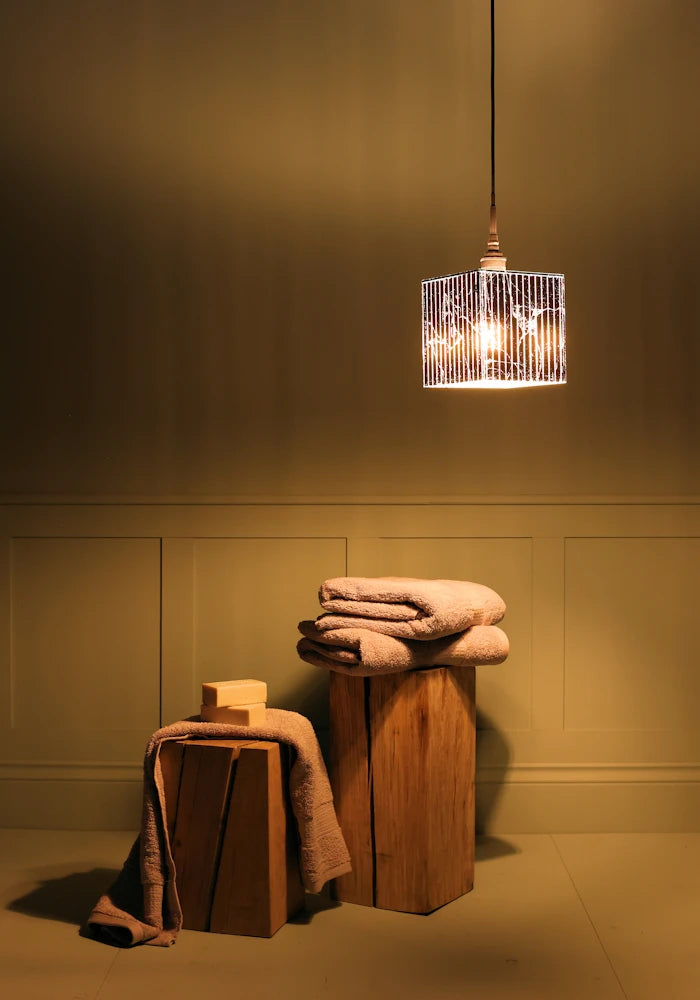 Large square silver leaf bathroom pendant light casting shadows onto bath towels.