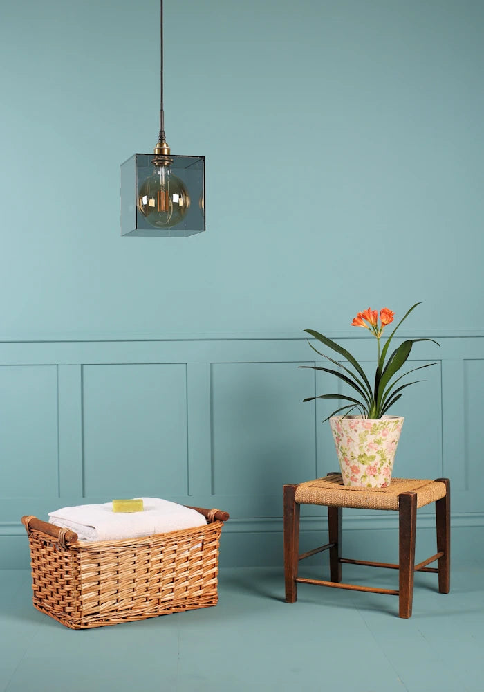 Large square smoked glass bathroom pendant light switched off, basket of bath towels and plant.