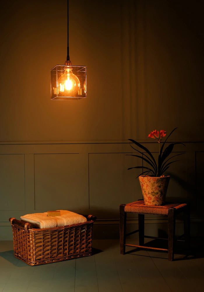 Large square smoked glass bathroom pendant light, basket of bath towels and plant.