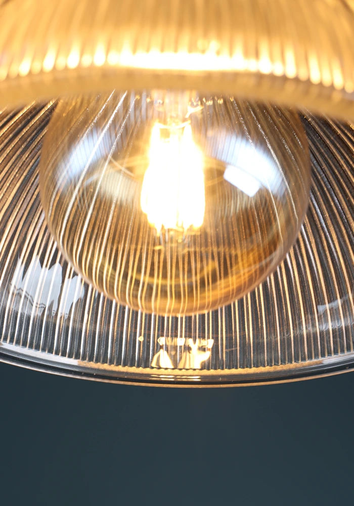 A close up image of a decorative warm LED light bulb in a ribbed glass bathroom pendant light shade