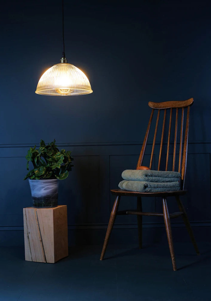 A large decorative ribbed glass dome bathroom pendant light with chair and plant