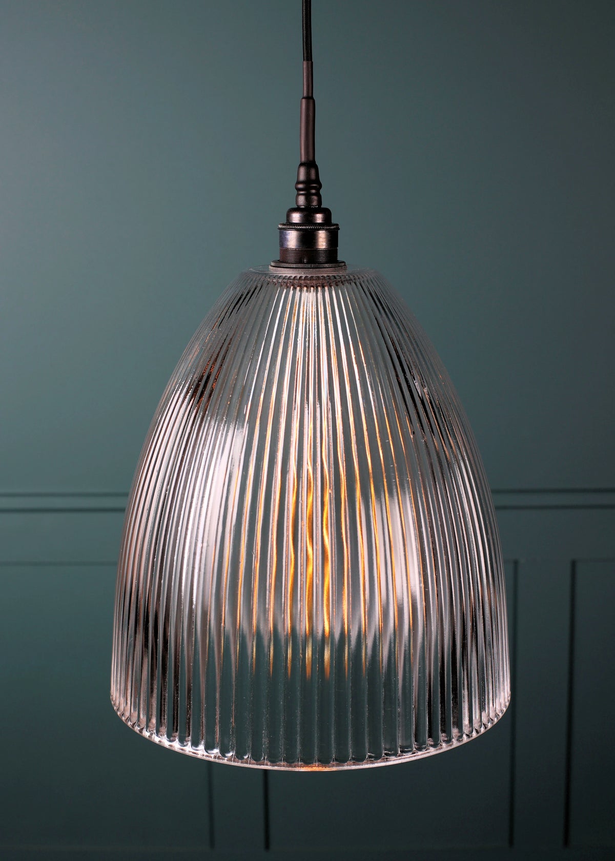 A ribbed glass pendant light with a warm glowing bulb inside, hanging against a dark teal paneled wall.