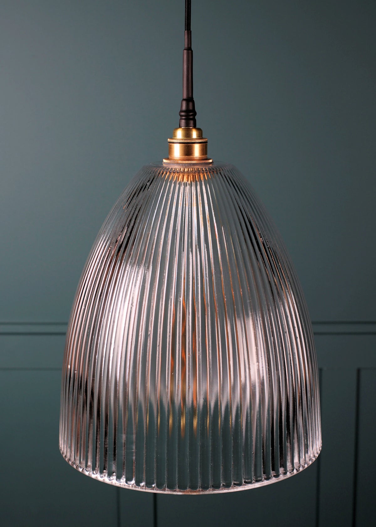 A ribbed glass pendant light with a warm glowing bulb inside, hanging against a dark teal paneled wall.
