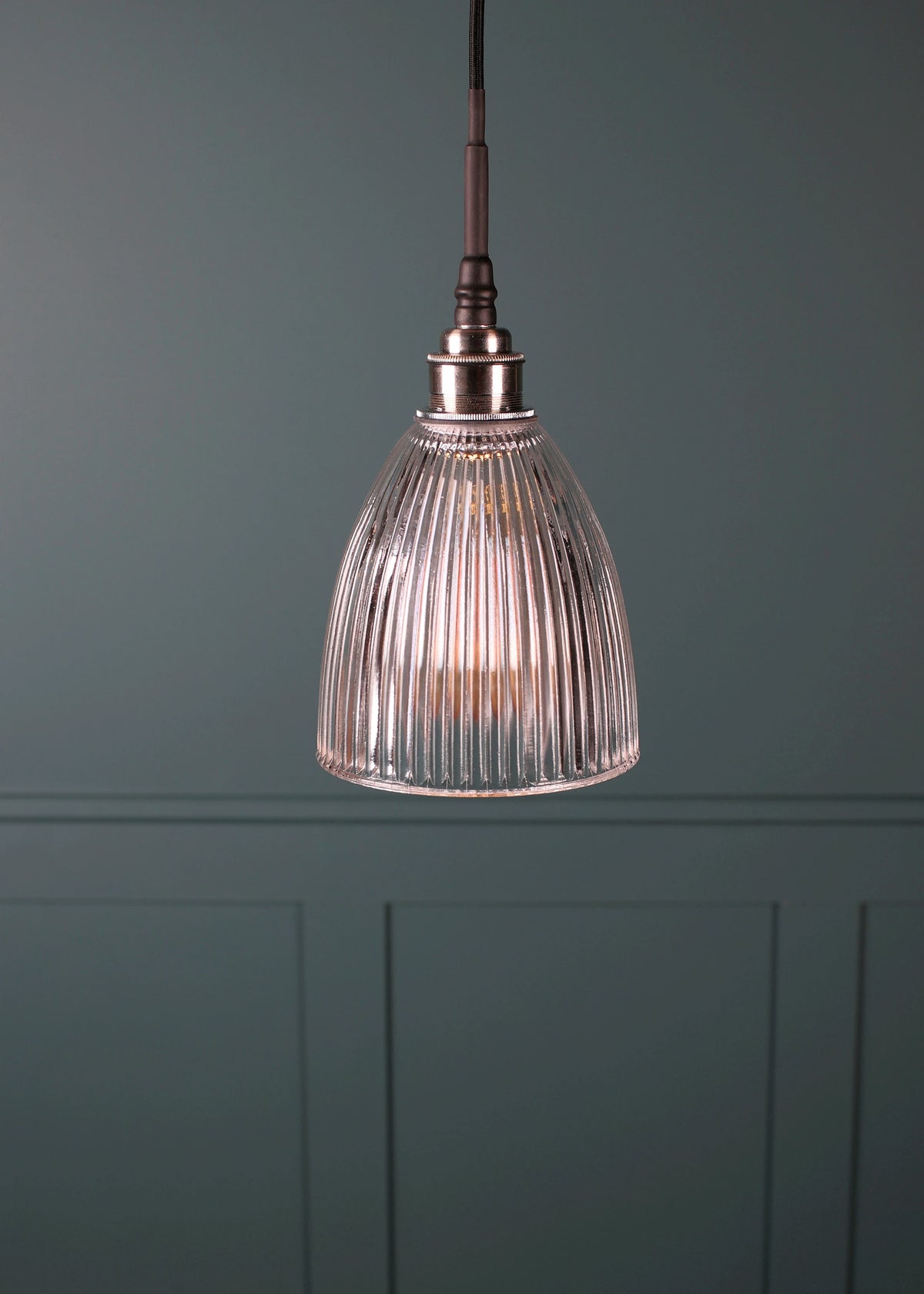 A single pendant light with a ribbed clear glass shade and a dark metal top fitting, hanging against a muted blue-gray paneled wall.