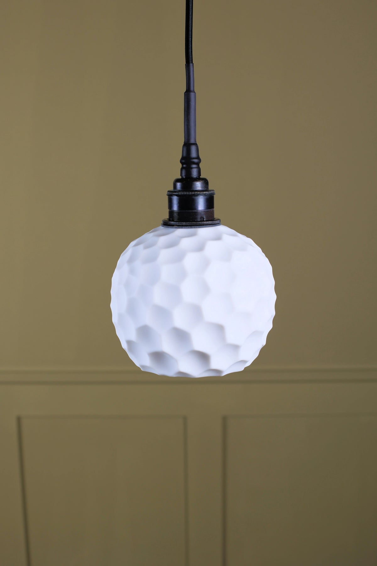 A ceramic beehive effect bathroom pendant light with bronze lamp holder on dark olive background