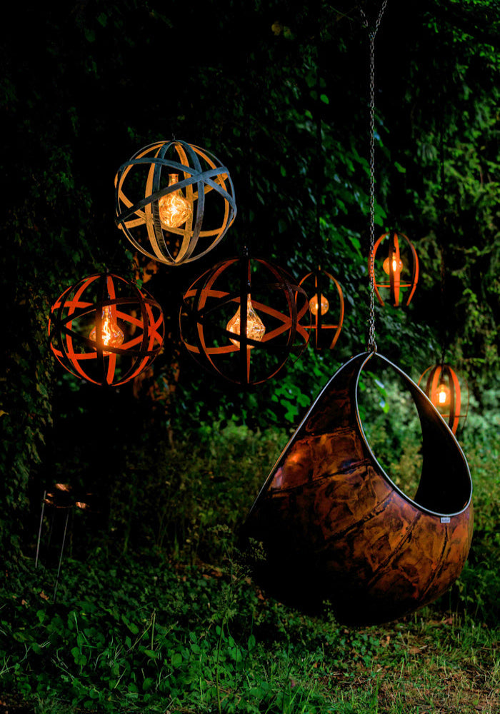 Large metal ornamental suspended outdoor lights in lush garden, hanging copper chair 