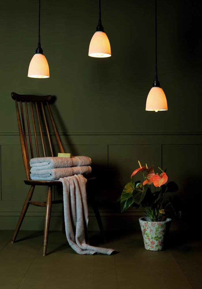 Triple porcelain cluster bathroom pendant light with wooden chair, bath towels and plant.