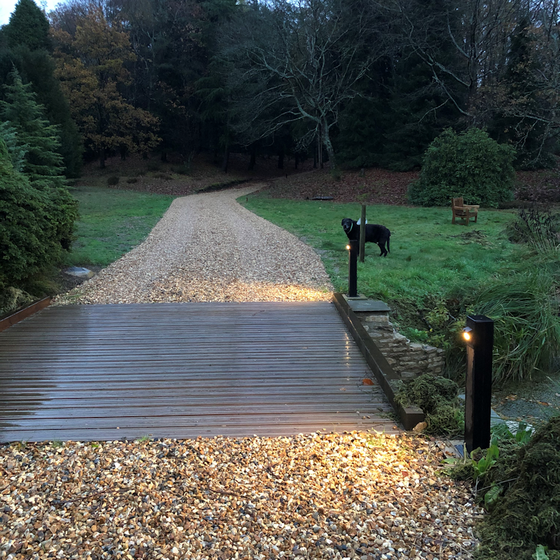Wooden LED path lights with stone driveway and black dog in background