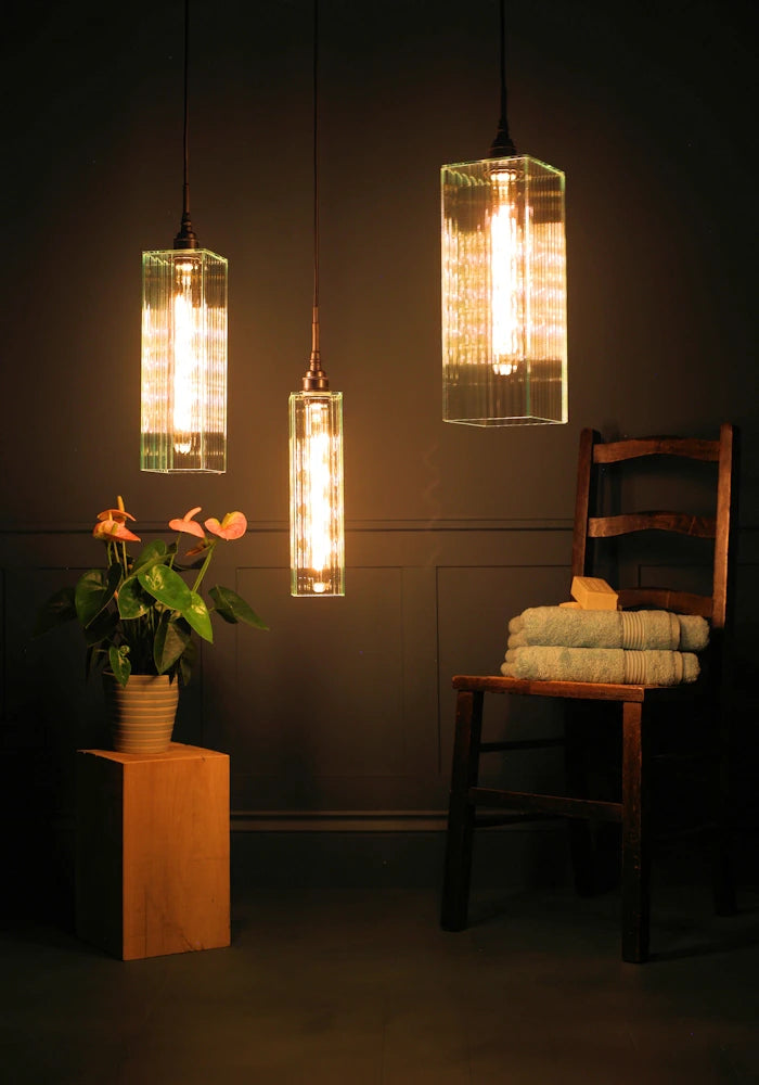 Triple large ribbed glass bathroom pendant light cluster with plant, wooden chair and towels.