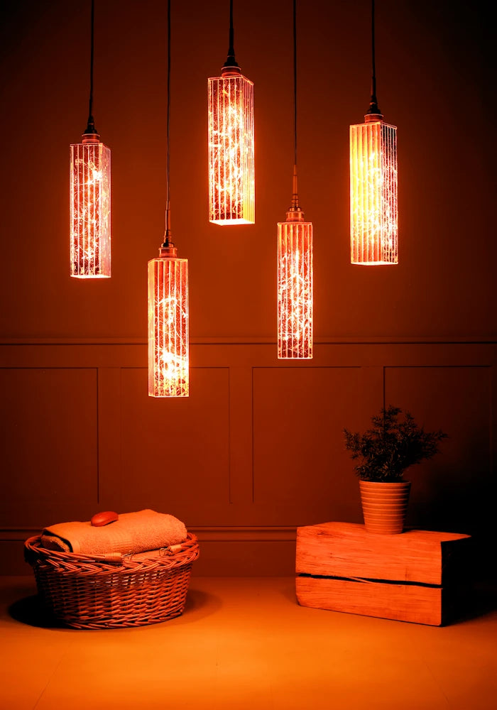 Cluster of five long rectangular copper leaf bathroom pendant lights, basket of bath towels and plant.