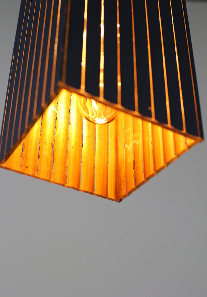 Close-up of a pendant light with black and gold striped shade on a gray background