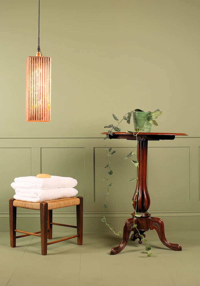 Large rectangular copper lead bathroom pendant light, bath towels and ornate table.