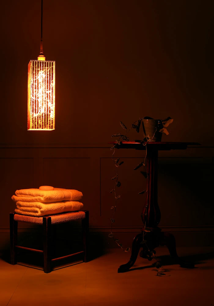 Large rectangular copper lead bathroom pendant light casting shadows, bath towels and ornate table.