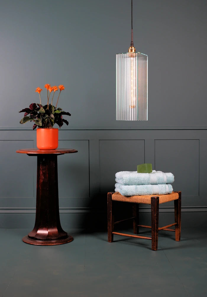 Large rectangular ribbed glass bathroom pendant light switched off with orange plant and bath towels.