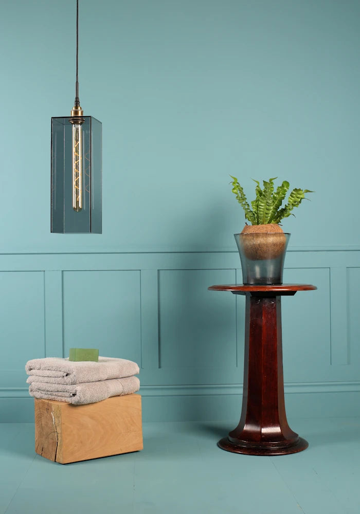 Large rectangular smoked glass bathroom pendant light switched off, bath towels and plant.