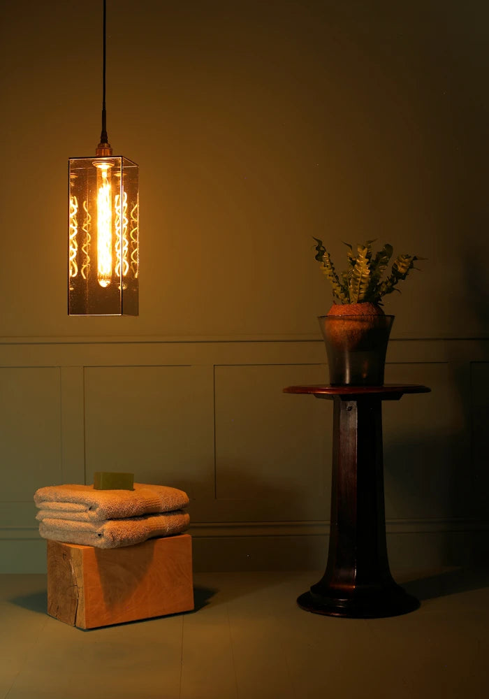 Large rectangular smoked glass bathroom pendant light, bath towels and plant.