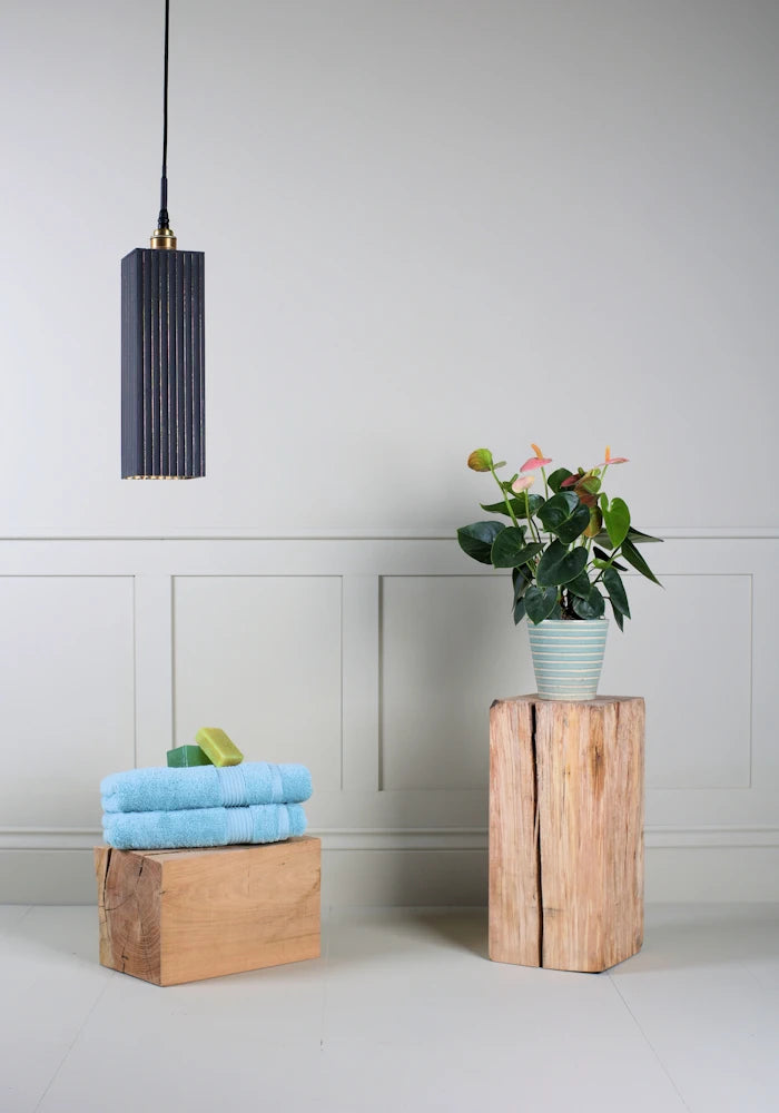 Black and gold leaf large bathroom pendant light switched off with bath towels and pot plant on wooden block.