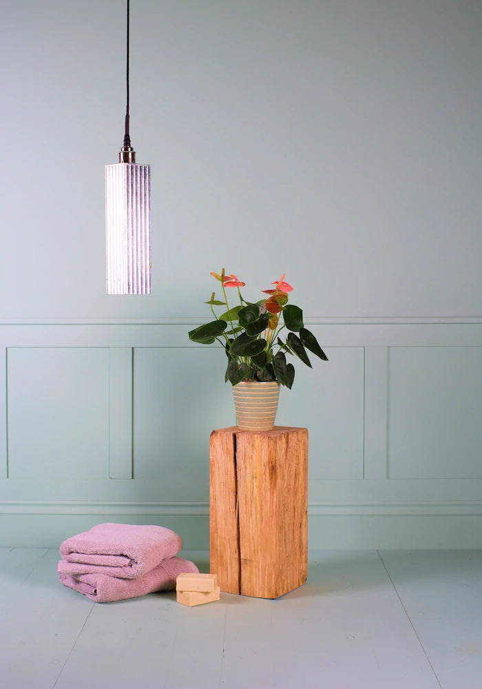 Long rectangular silver leaf bathroom pendant light with bath towels and pot plant.