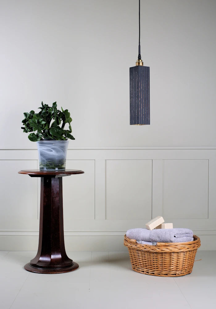 Elegant long rectangular black and gold bathroom pendant light switched off with plant and basket of bath towels.