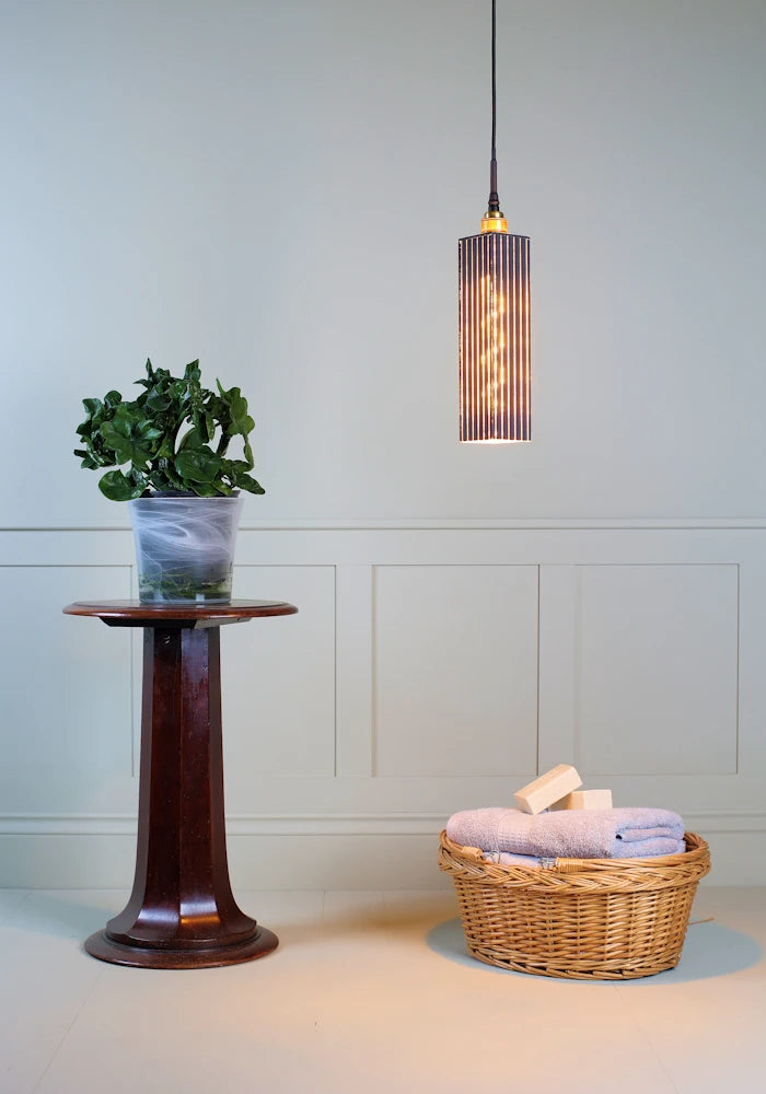 Elegant long rectangular black and gold bathroom pendant light with plant and basket of bath towels.