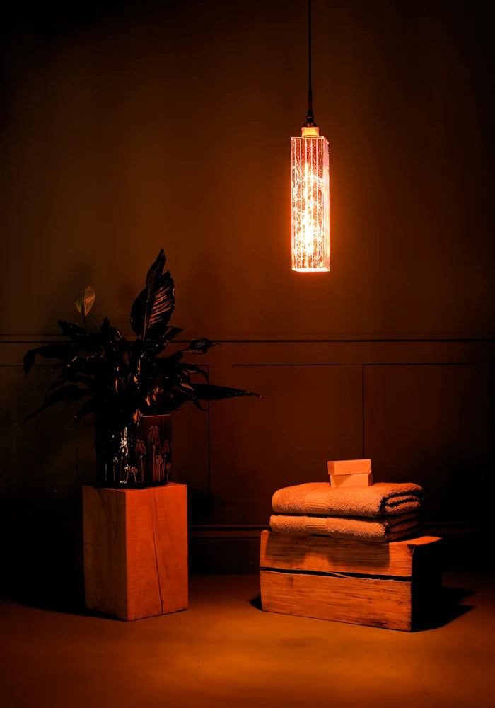 Elongated copper leaf bathroom pendant light, plant and bath towels.