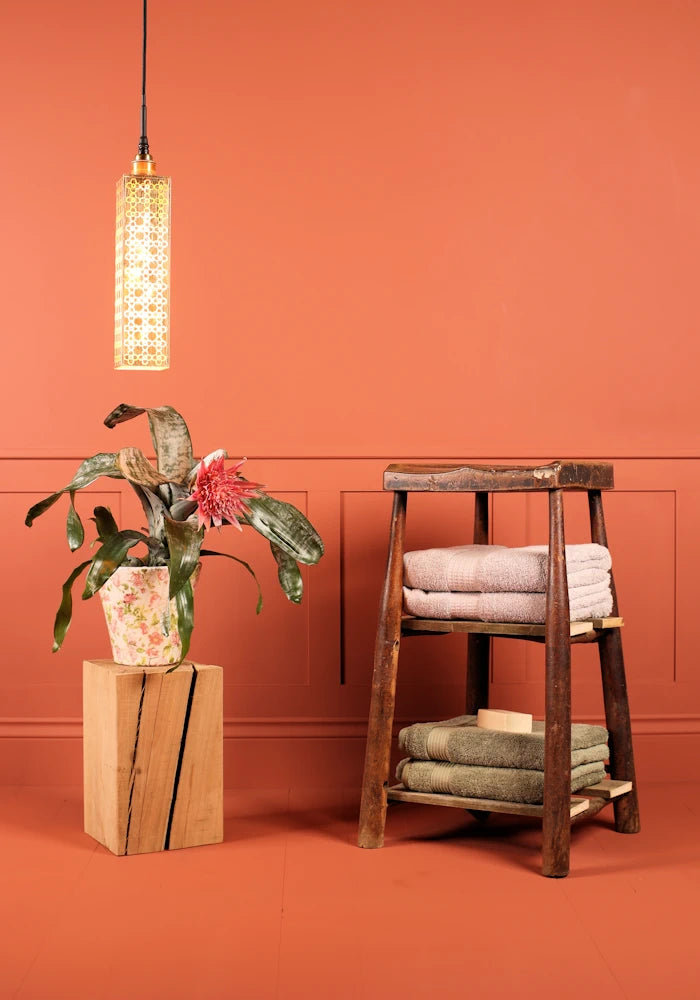 Elongated rectangular Moroccan style bathroom pendant light, plant and wooden stool with bath towels. 