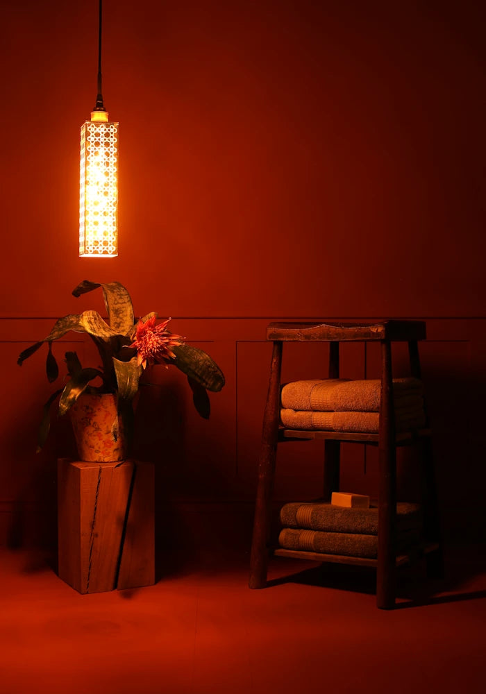 Elongated rectangular Moroccan style bathroom pendant light, plant and wooden stool with bath towels. 