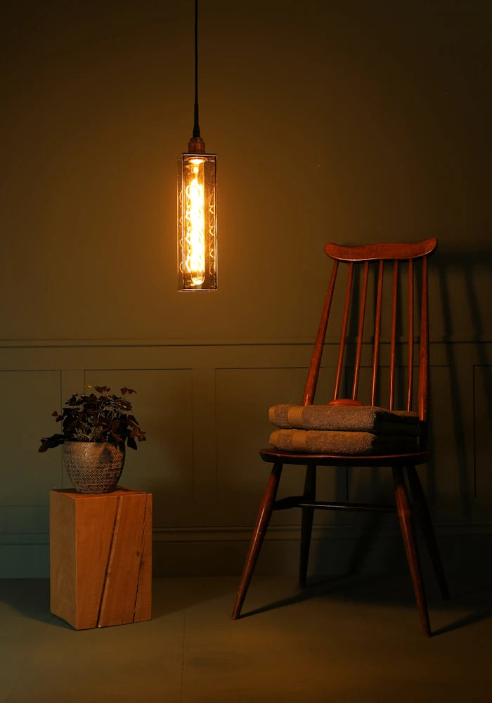 Elongated rectangular smoked glass bathroom pendant light casting shadows, plant, wooden chair and bath towels.