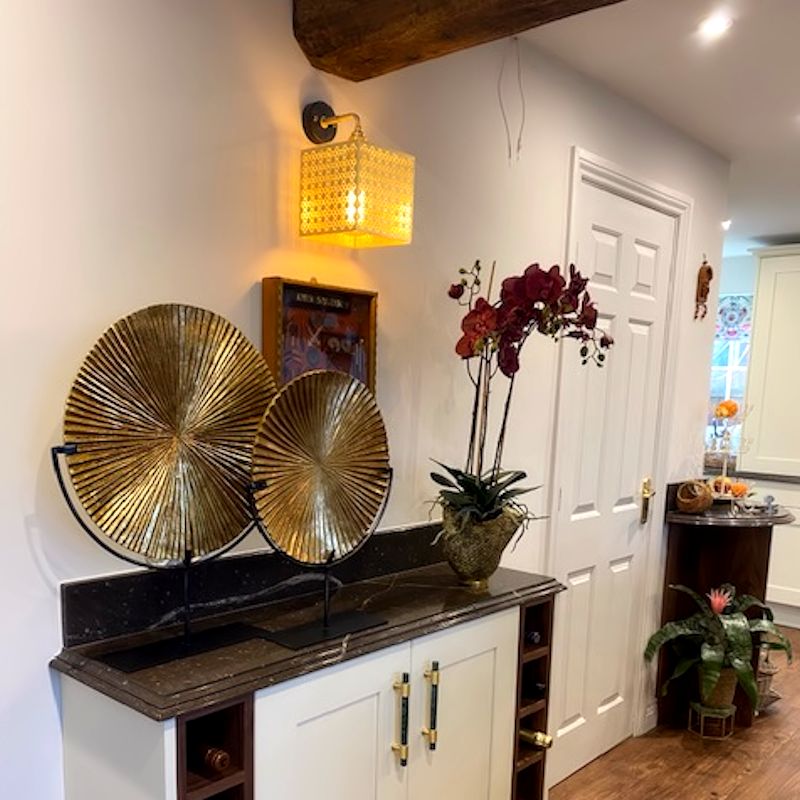 Modern dresser with gold leaf wall light, white cabinets, black countertop, and decorative elements.