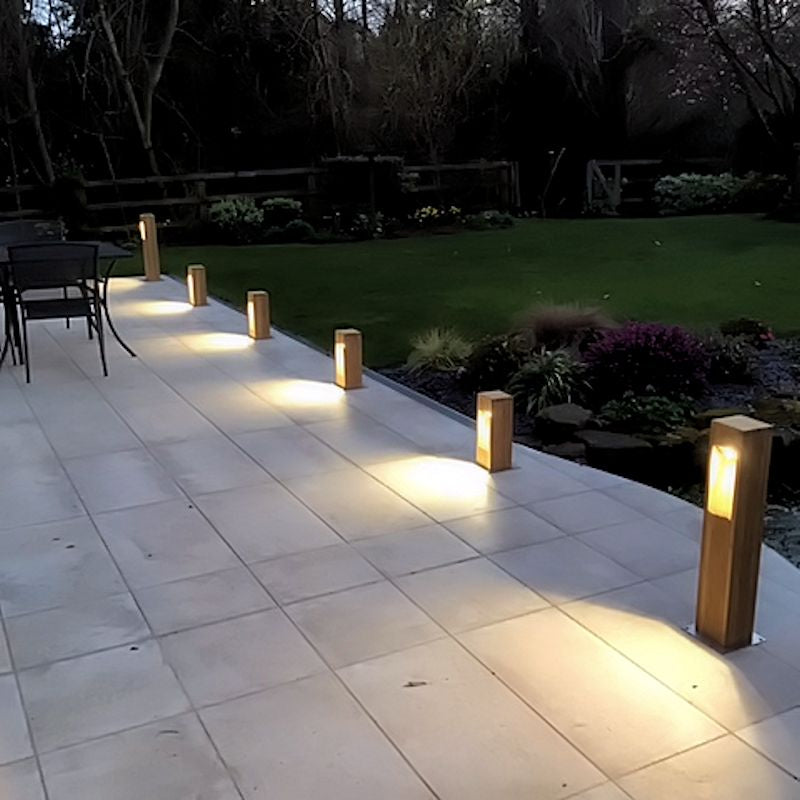 Wooden outdoor bollard lights on patio with white floor tiles and garden in background